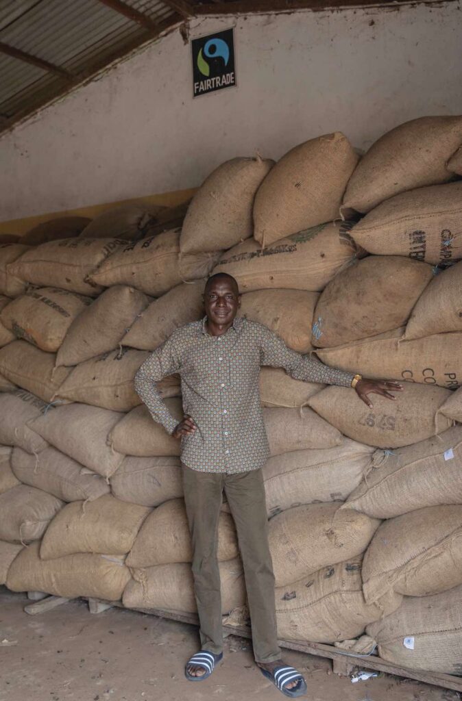 Bengaly Bourama in front of stacks of sacks of cocoa